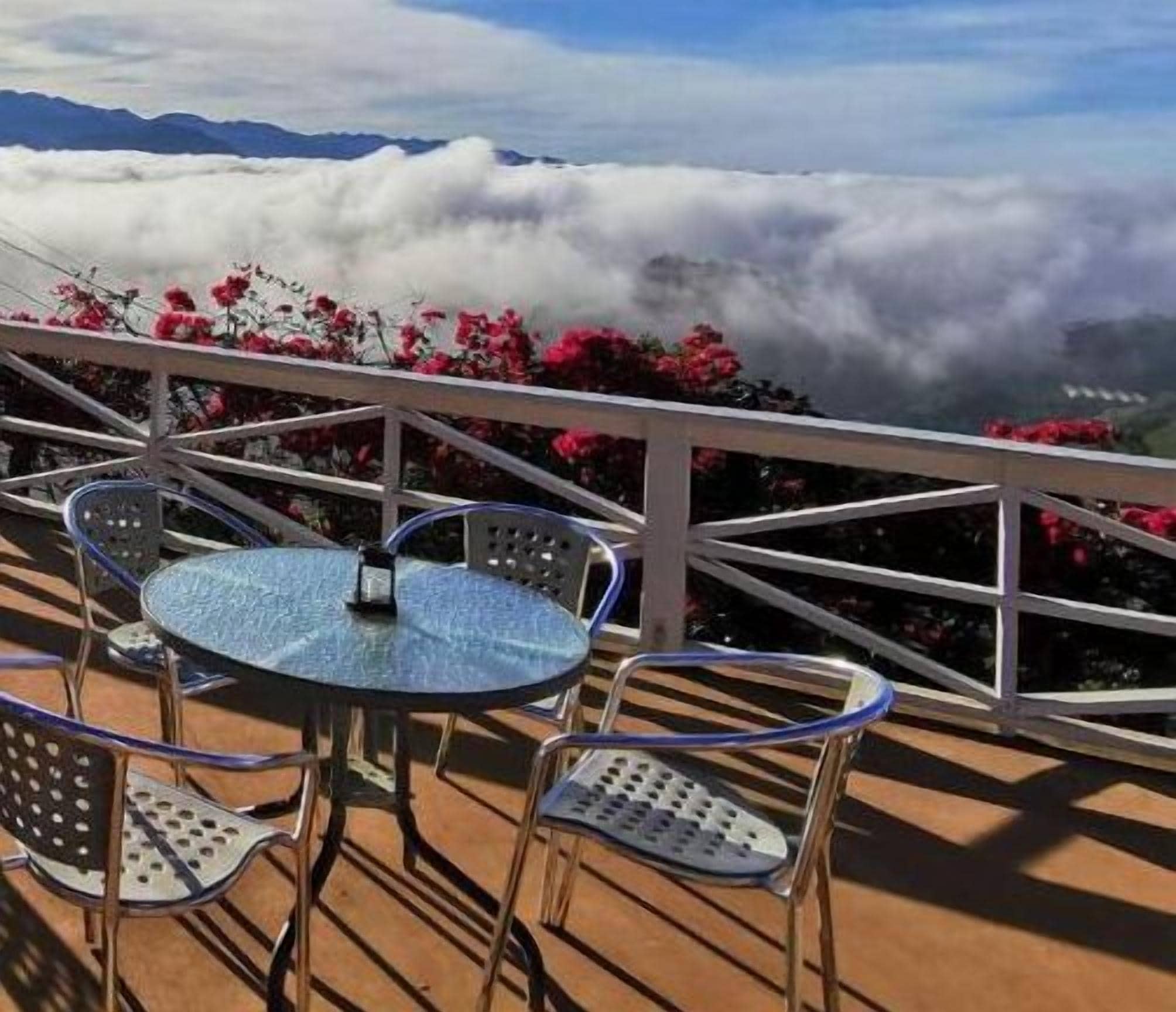 Een terras met een ronde tafel en stoelen, met uitzicht op een bergachtig landschap met wolken eronder.