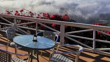 Een terras met een ronde tafel en stoelen, met uitzicht op een bergachtig landschap met wolken eronder.