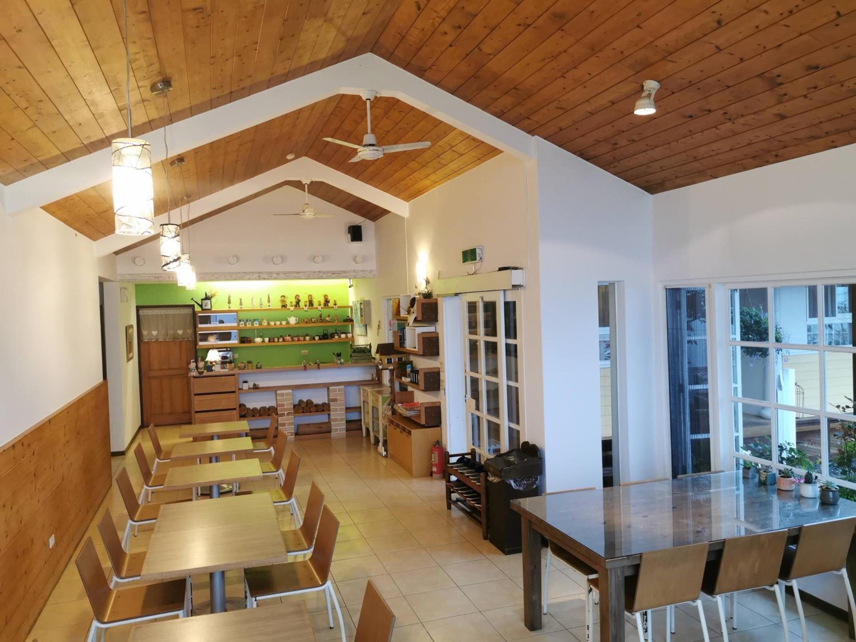 Un comedor amplio con mesas y sillas de madera, una cocina al fondo y vistas a través de grandes ventanales.