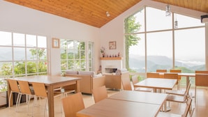 A spacious dining area with wooden tables and chairs, large windows offering a view of the mountains, and a fireplace with decorative items. - Alishan Tea Garden (Fanlu)