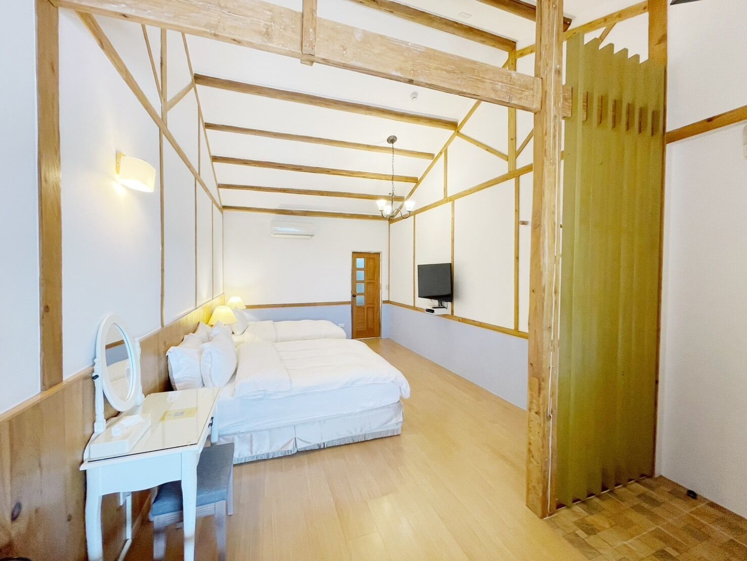 Un dormitorio con techo de madera, una cama, un escritorio con espejo, un televisor y una puerta.