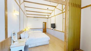 A bedroom with a wooden ceiling, a bed, a desk with a mirror, a TV, and a door.