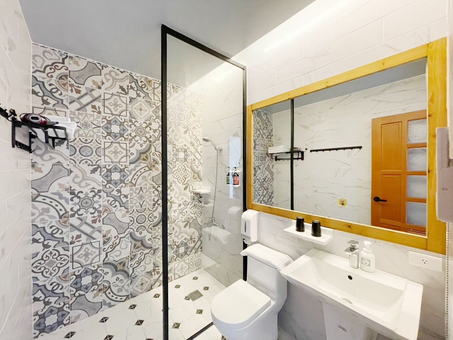 Un baño con baldosas estampadas, una ducha, un inodoro, un lavabo y un espejo con marco de madera.