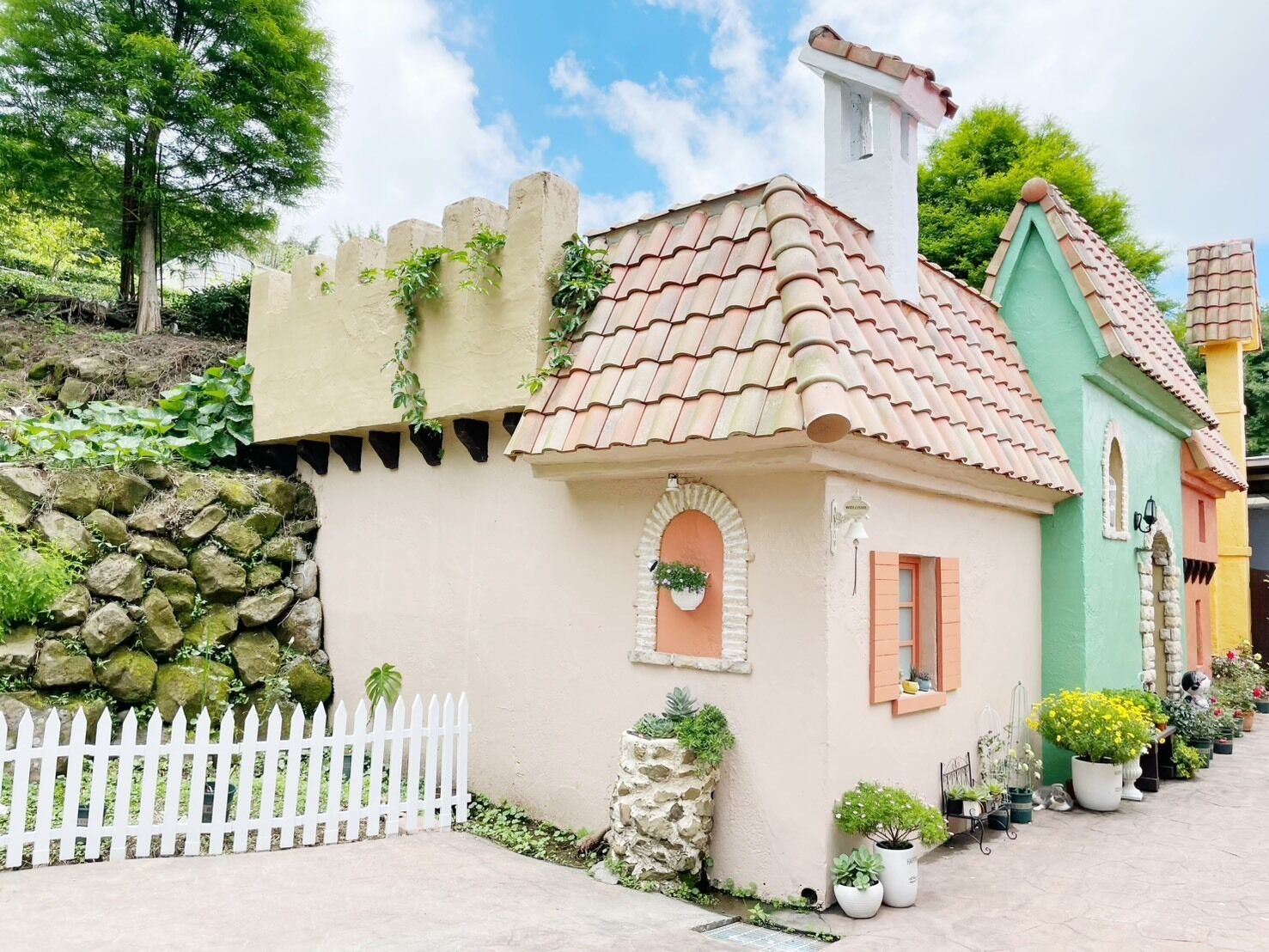 A quaint building with a tiled roof, a stone wall, and a white picket fence.