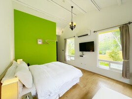 Un dormitorio con una pared de acento verde, una cama, un televisor y una ventana con cortinas.