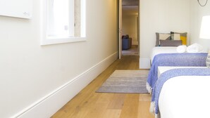 Une chambre d’hôtel avec un plancher en bois, une grande fenêtre, un lit recouvert d’une couverture bleue et une table de chevet.