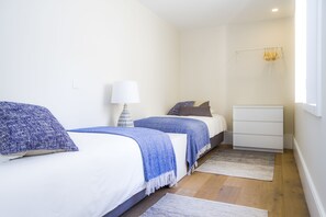 Ein Schlafzimmer mit zwei Betten, einem Nachttisch mit Lampe, einem Schminktisch und einem Fenster mit Vorhängen.