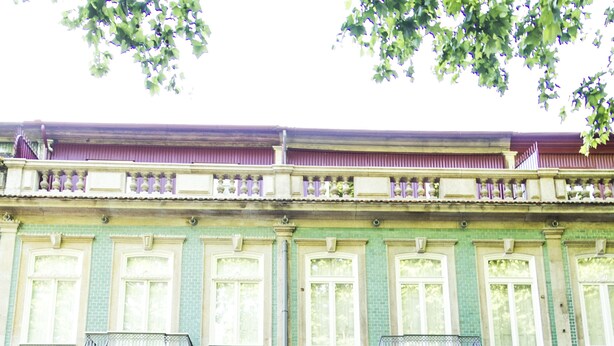 Un bâtiment doté d’une façade verdoyante, de grandes fenêtres et d’une entrée centrale avec une porte décorative.