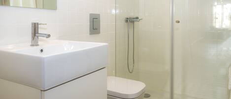 Une salle de bain avec un lavabo blanc, des toilettes et une douche séparée par une paroi de verre.