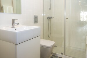 A bathroom with a white sink, a toilet, and a glass-enclosed shower area. - Liiiving in Porto - Central Garden Flat (Porto)