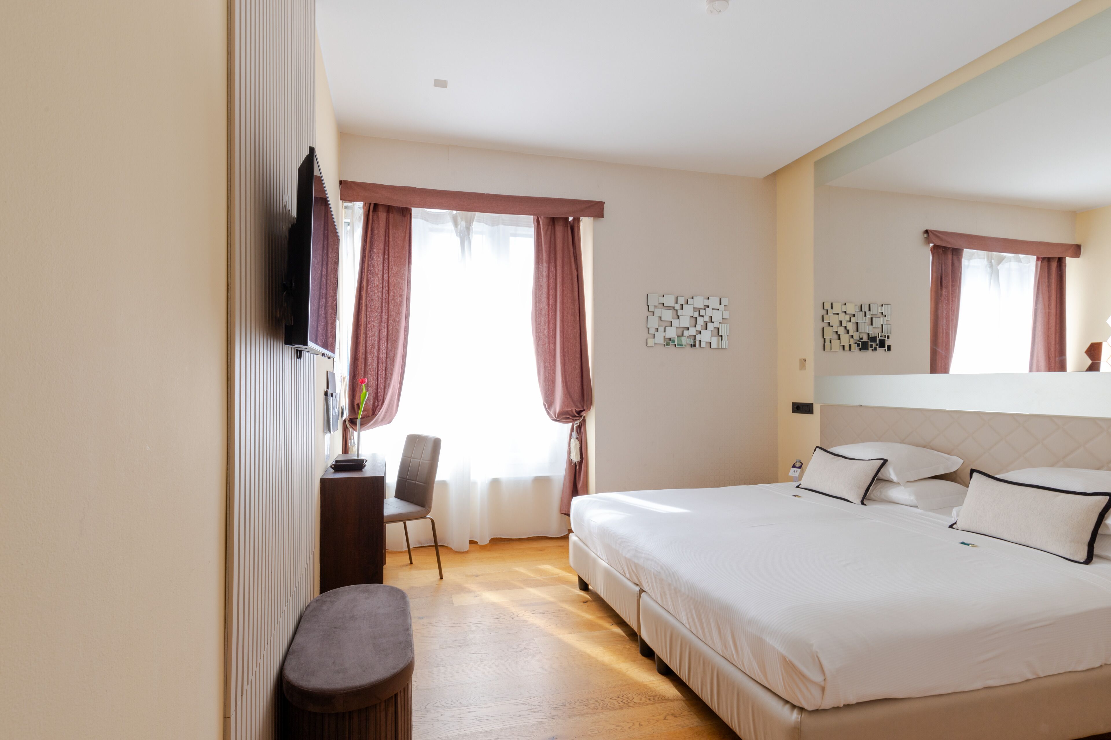 Ein Hotelzimmer mit einem großen Bett, einem Schreibtisch mit Stuhl, einem Fernseher und einem Fenster mit Vorhängen.