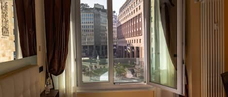 A hotel room with a large window, a bed, a nightstand, and a radiator.