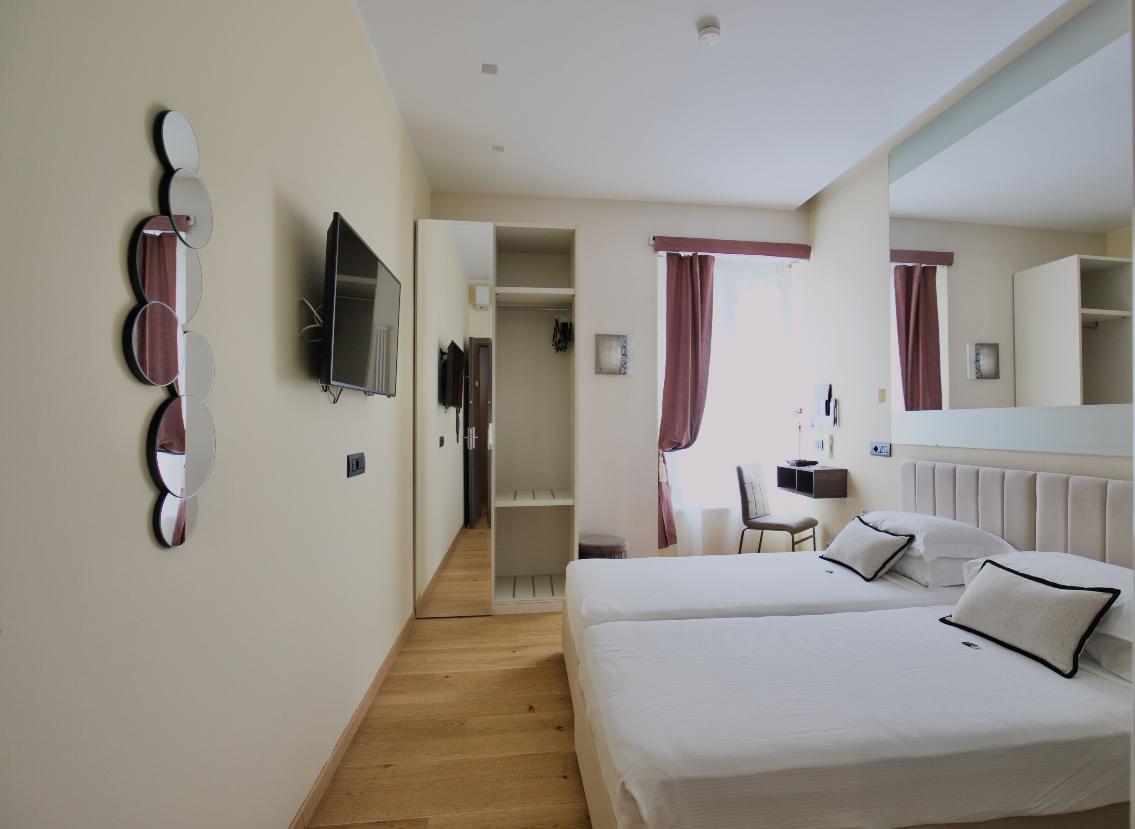 Habitación de hotel con dos camas, un televisor, un espejo y un escritorio con una silla.