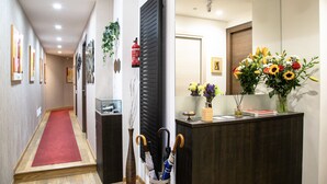 A hallway with a red carpet, a reception desk with a vase of flowers, and a fire extinguisher mounted on the wall. - AH - Fashion District (Milan)