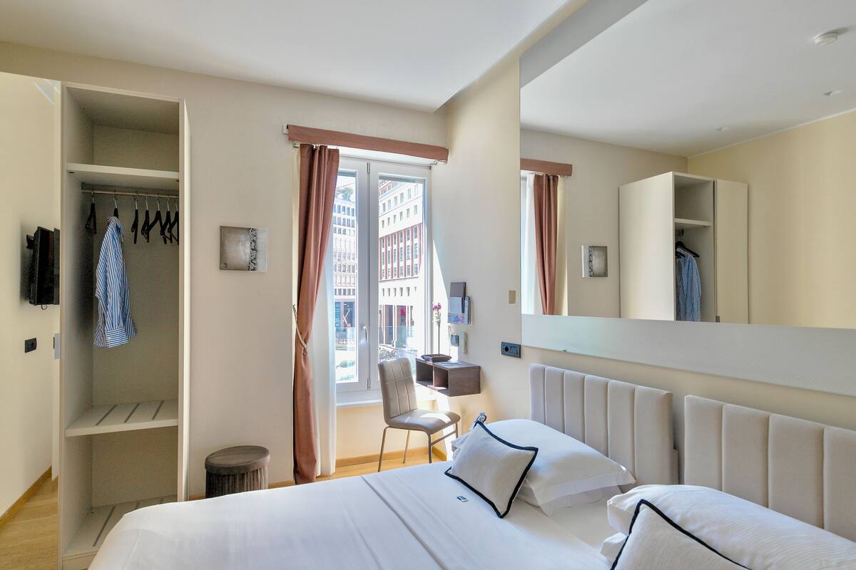 A hotel room with a bed, a chair, a wardrobe, and a window with curtains.