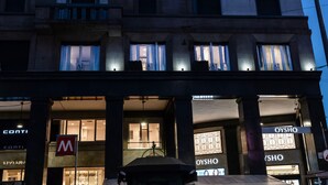 A multi-story building with illuminated signage for 'AI' and 'OYSHO' stores. - AH - Fashion District (Milan)