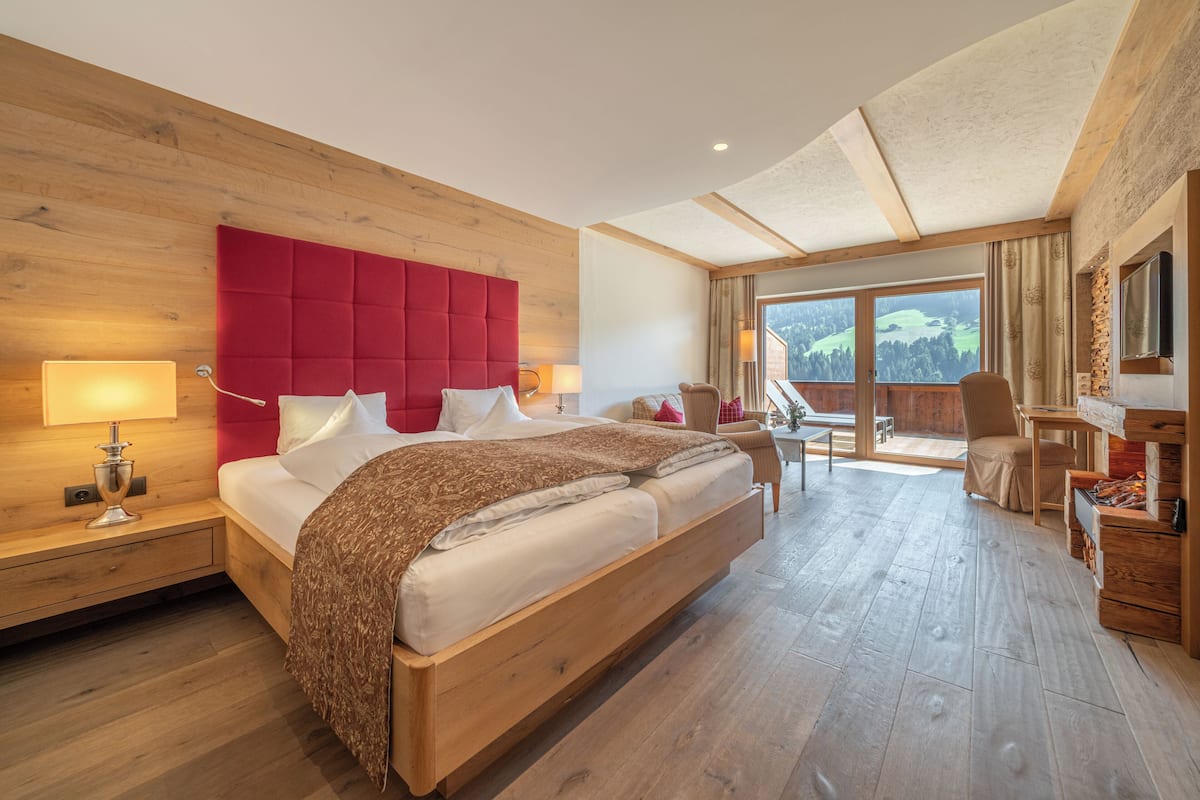 A hotel room with a large bed, wooden headboard, two bedside tables with lamps, a desk, and a chair.
