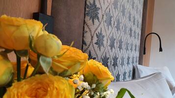 Ein Blumenstrauß aus gelben Rosen auf einem Tisch, im Hintergrund eine Wand mit Muster und eine moderne Leuchte.