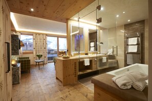 A modern bathroom with a large mirror, a bathtub, and a wooden floor. - Alpbacherhof – Mountain & Spa Resort (Alpbach)
