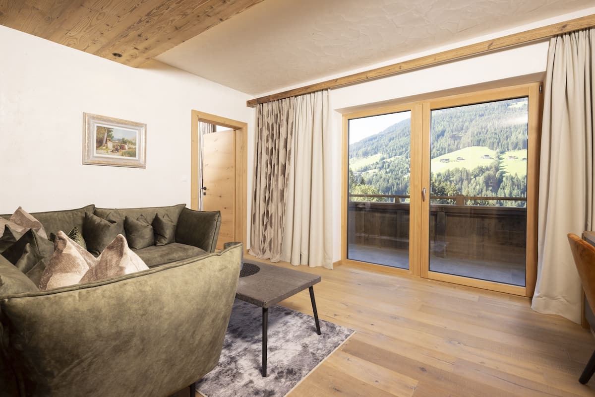 A living room with a green sofa, a small table, and a view of a mountainous landscape through large glass doors.