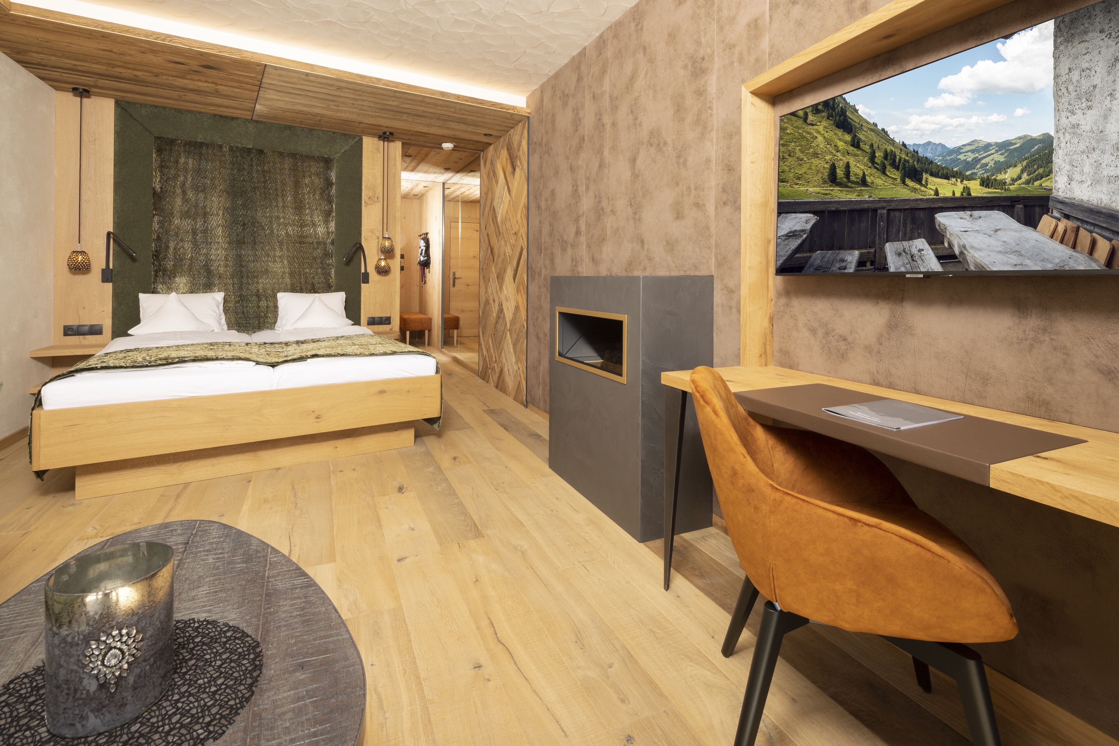 A bedroom with a bed, a desk, a chair, a fireplace, and a view of the outdoors.