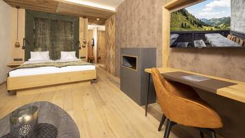 A bedroom with a bed, a desk, a chair, a fireplace, and a view of the outdoors.