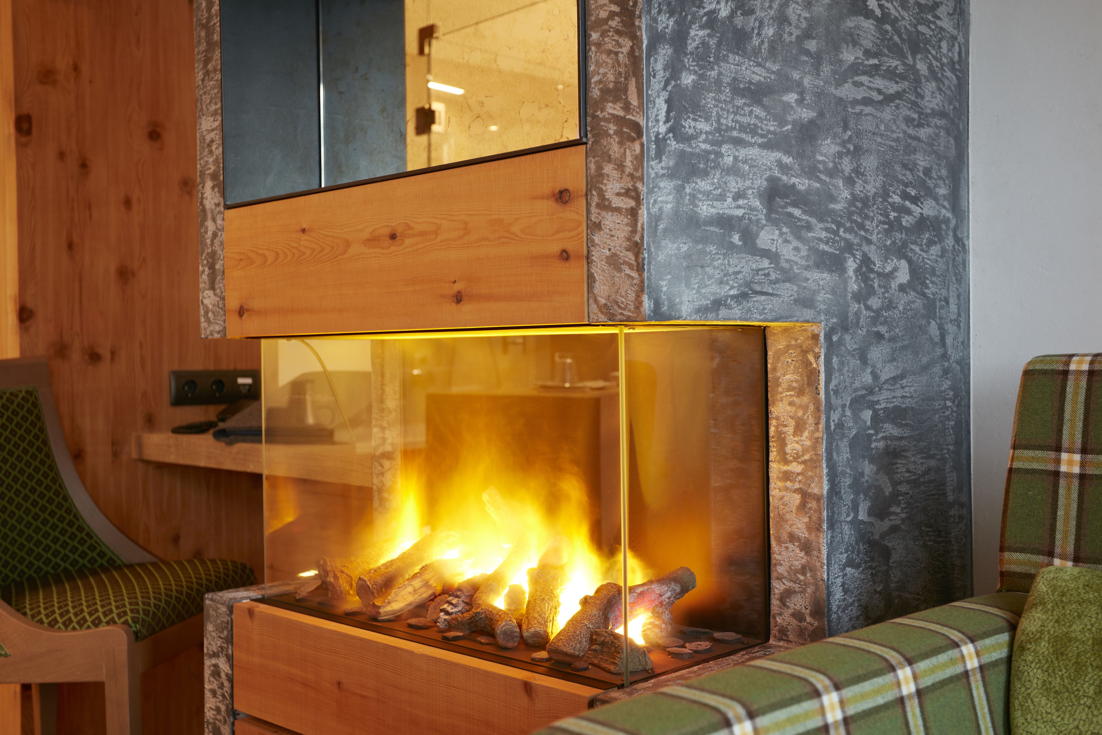 A modern interior with a glass-fronted fireplace, wooden paneling, and a plaid-patterned chair.