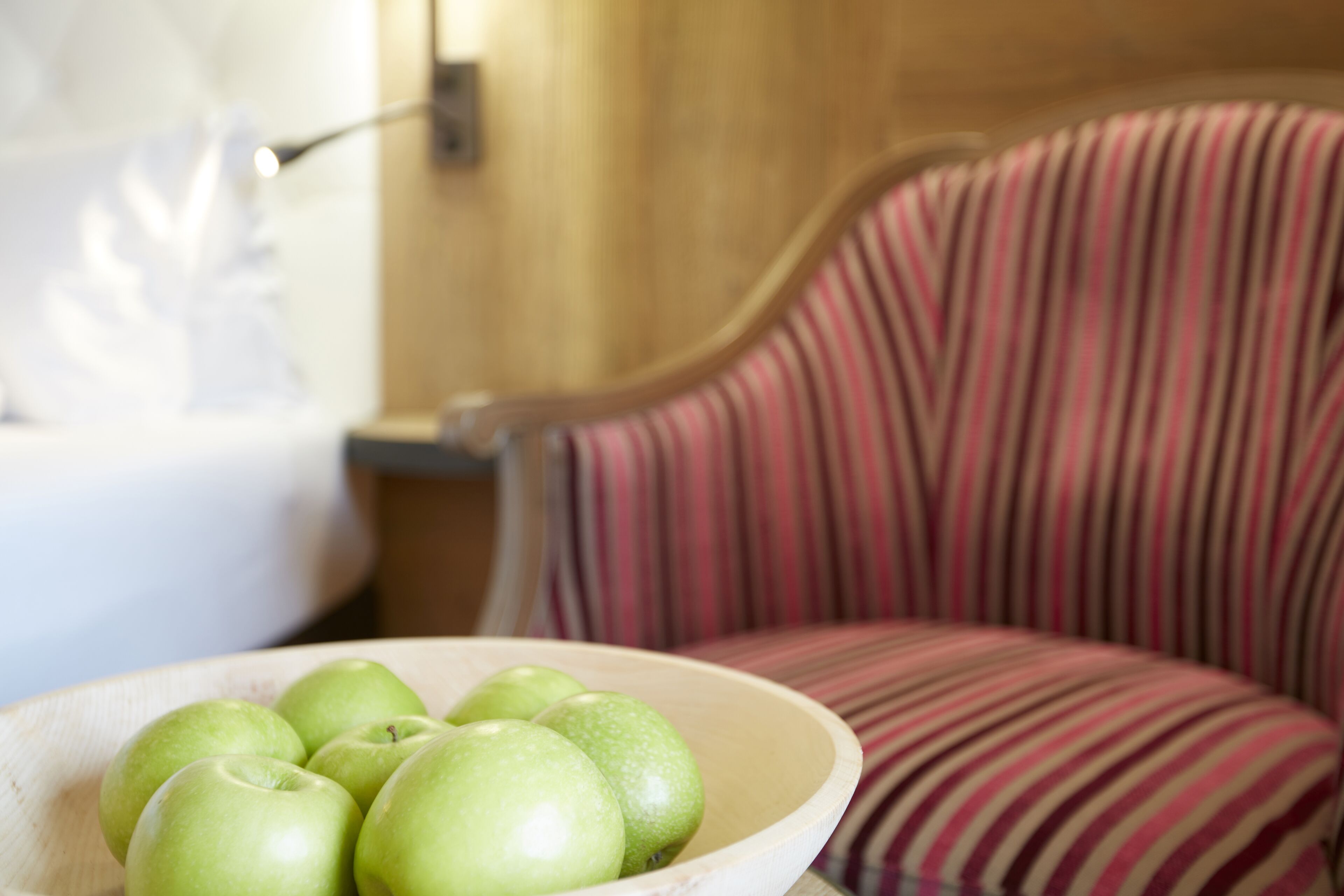 A bowl of green apples on a wooden table next to a striped chair.