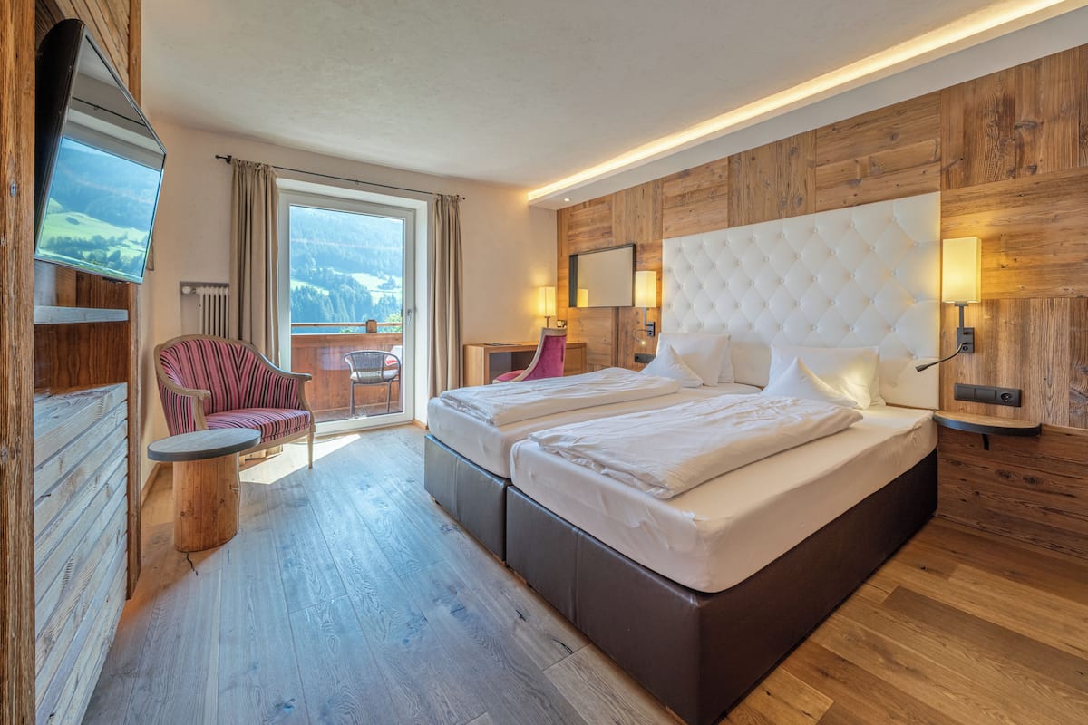 A hotel room with a large bed, a chair, a small table, a TV, and a view of the mountains.