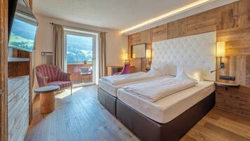A hotel room with a large bed, a chair, a small table, a TV, and a view of the mountains.