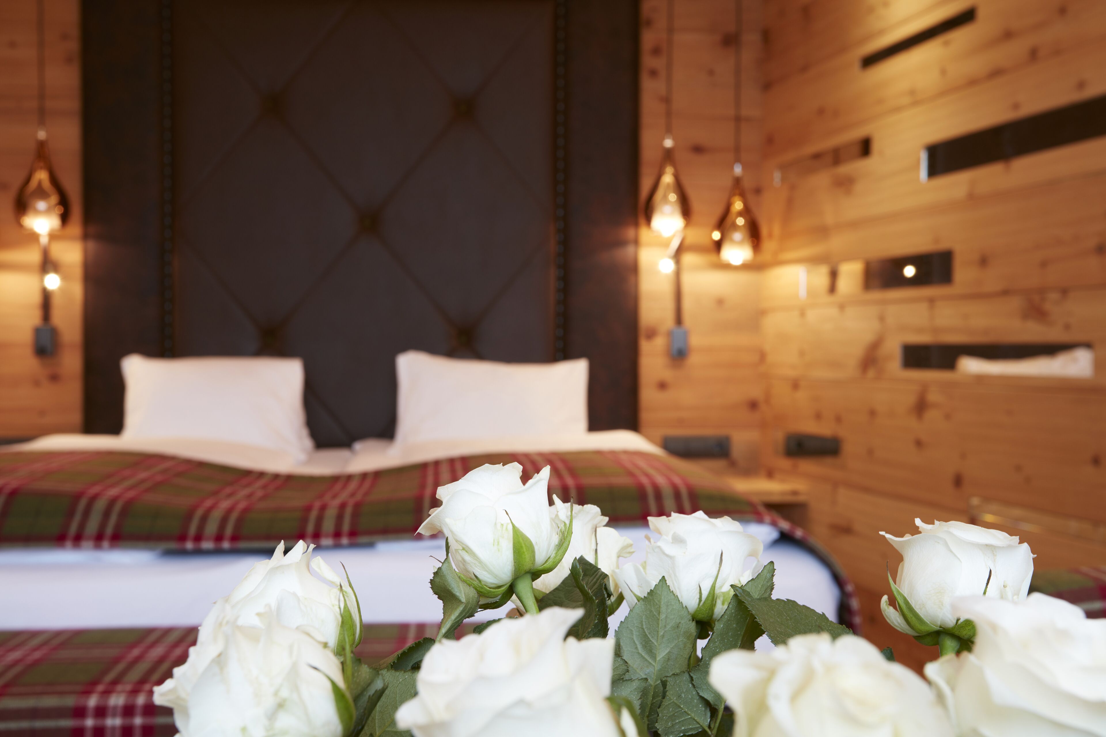A bedroom with a bed, wooden walls, and hanging light fixtures.