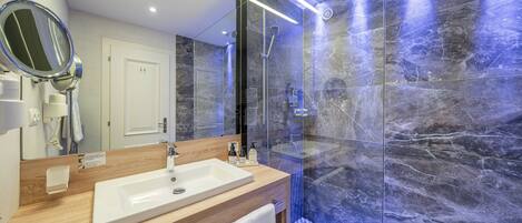 A modern bathroom with a large mirror, a sink, a shower, and marble walls.