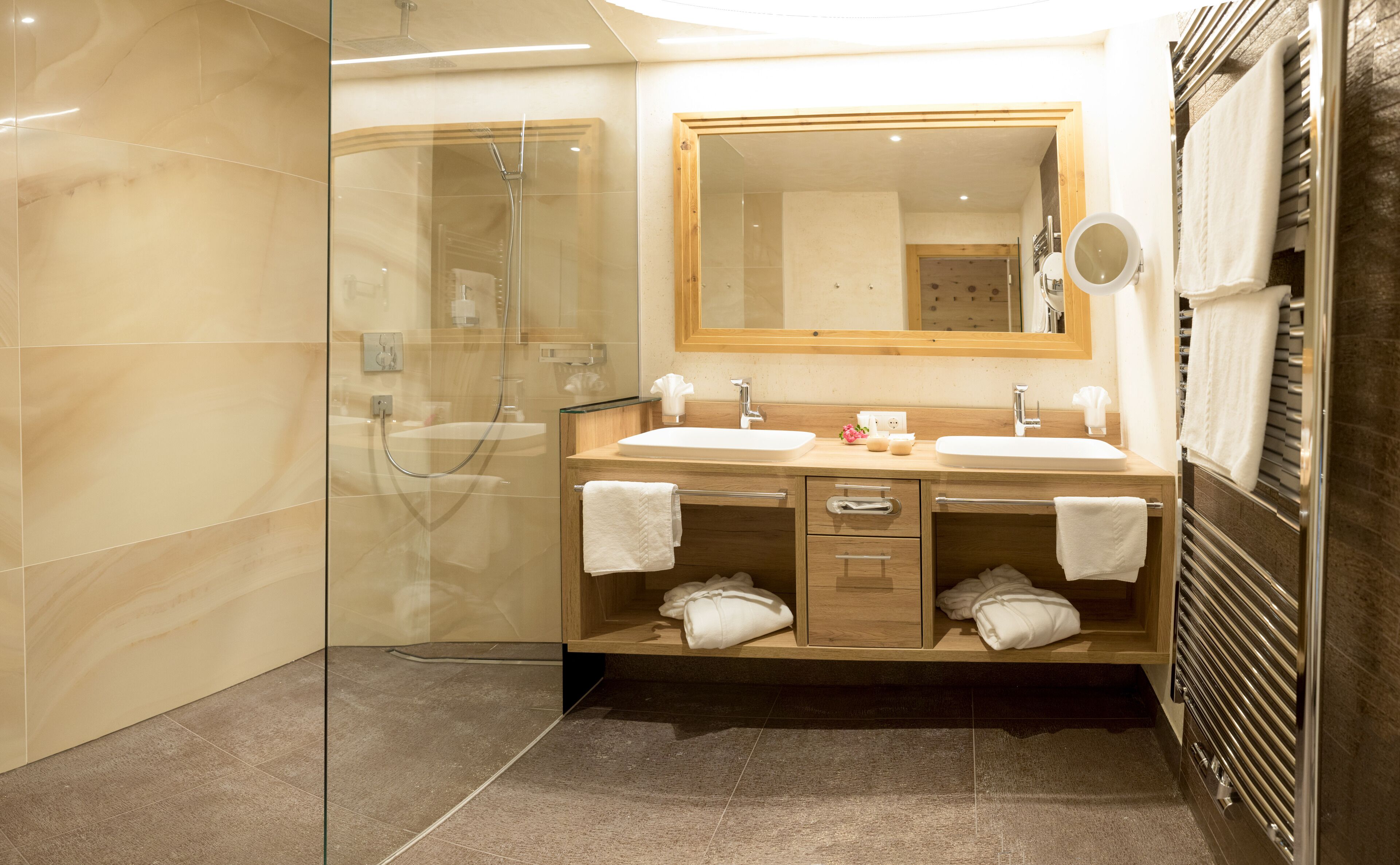 A modern bathroom with two sinks, a glass shower enclosure, and a wooden vanity with towels.