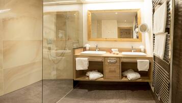 A modern bathroom with two sinks, a glass shower enclosure, and a wooden vanity with towels.