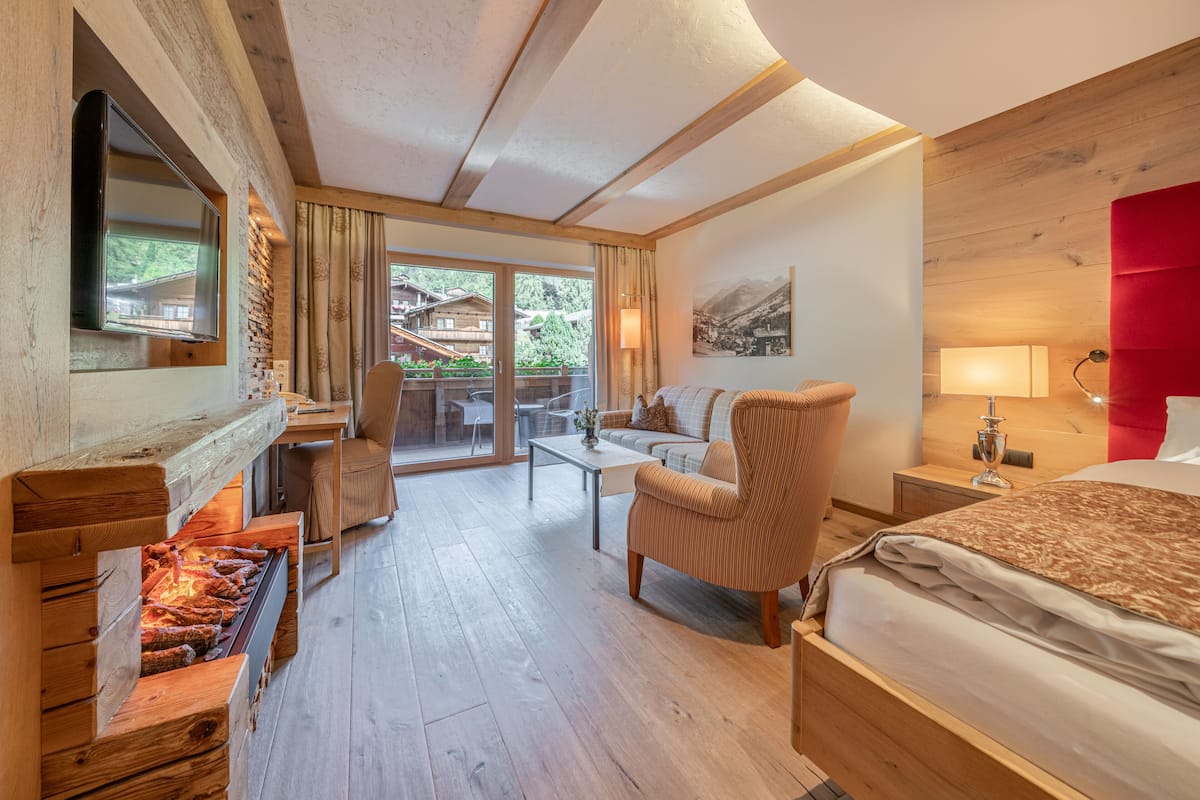 A hotel room with a fireplace, a sofa, a bed, a TV, and a view of the outdoors.