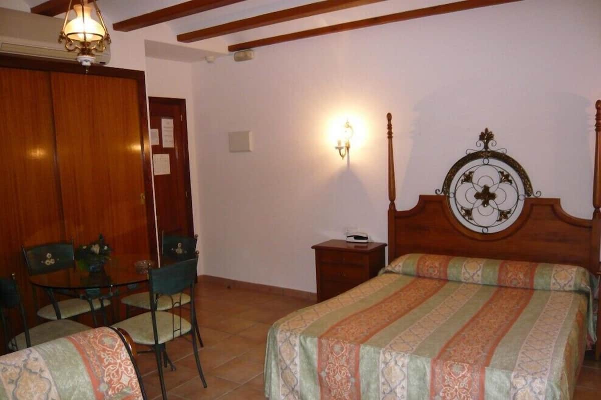 A hotel room with two beds, a wooden headboard, a nightstand, a chair, a desk, and a wall-mounted lamp.