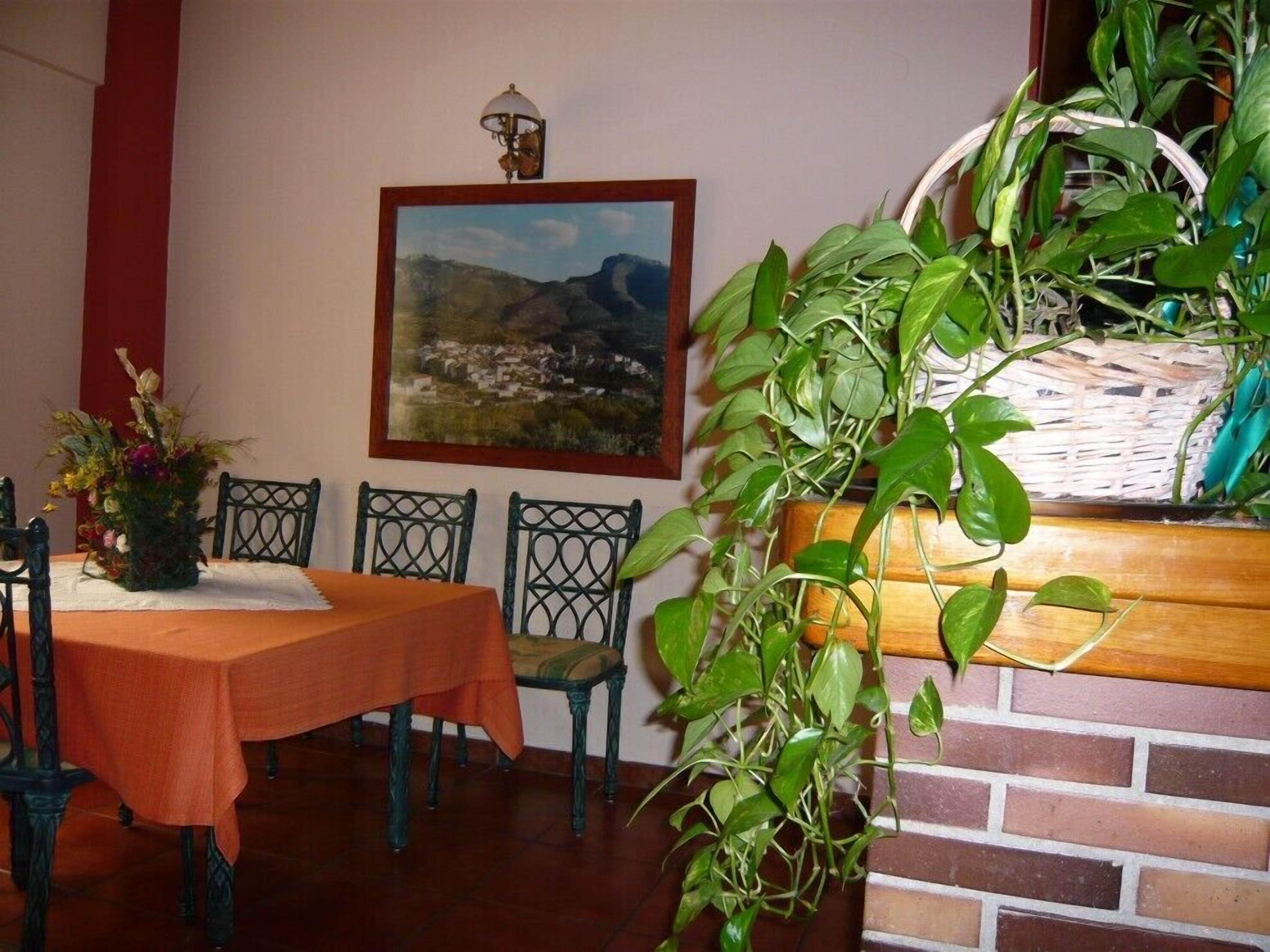 A dining area with a table set for four, a painting on the wall, and a large potted plant.