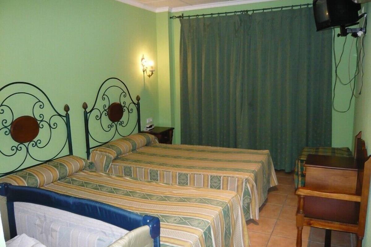 A room with two beds, a desk, a chair, a television, and a curtain.