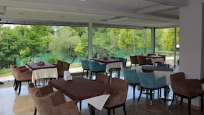 Un restaurante con terraza al aire libre que da a un lago, con muebles modernos y ventanas amplias.