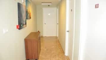 A narrow hallway with a wooden bench, a door at the end, and a wall-mounted light fixture.
