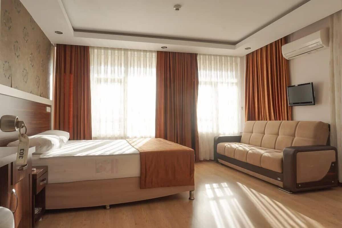 Una habitación de hotel con cama, sofá, televisor y aire acondicionado.