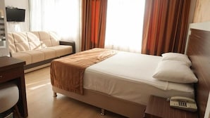 Una habitación de hotel con cama, escritorio, silla, televisor y cortinas.