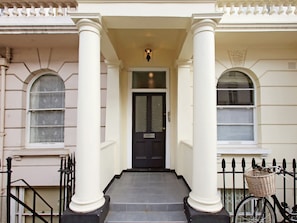 A building entrance with white columns, a black door, and a bicycle with a basket. - Central London Flat Westminster (London)