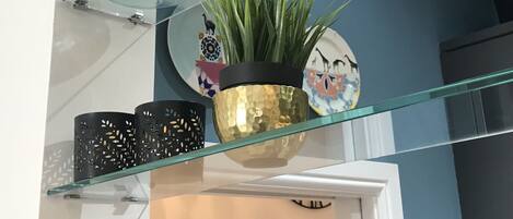 A glass shelf with decorative items including a vase, a potted plant, and a plate with animal illustrations.