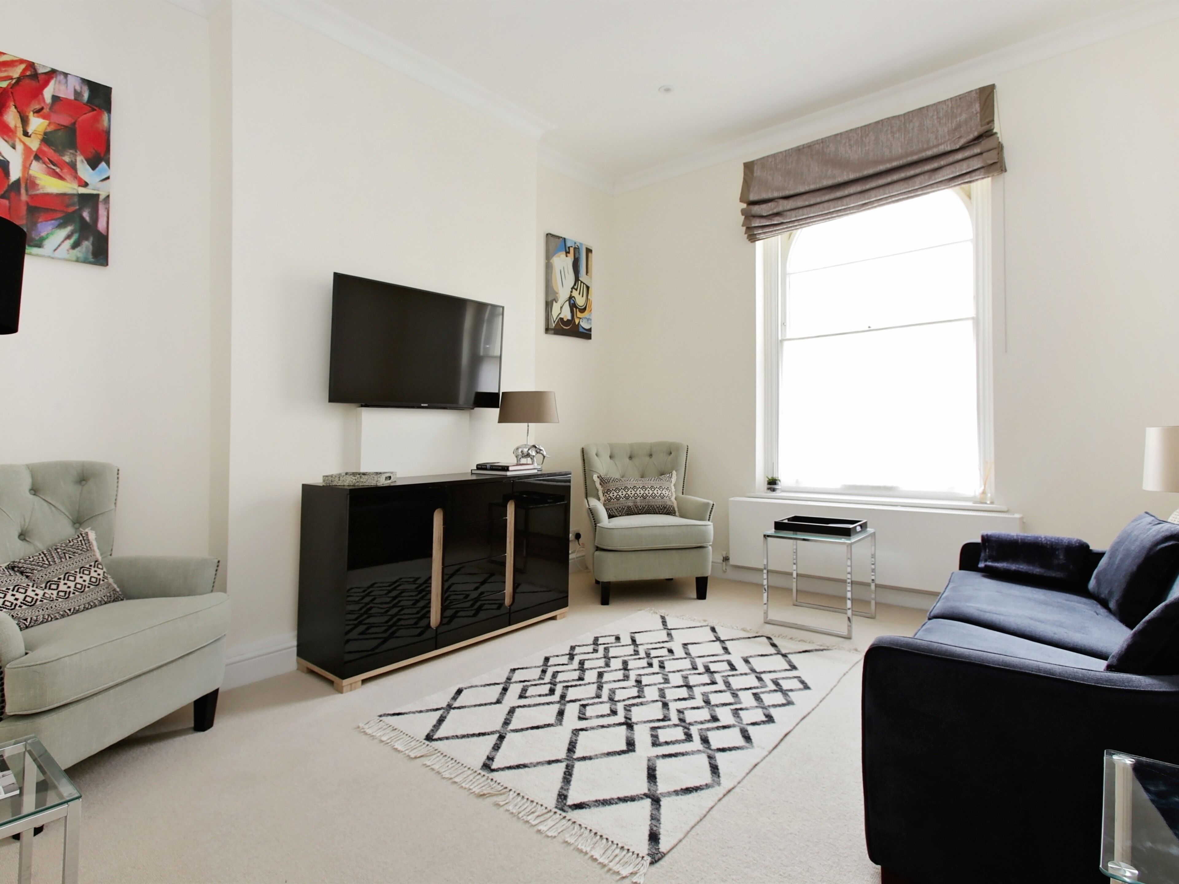 A modern living room with a grey sofa, a black entertainment unit, a beige armchair, and a patterned rug.