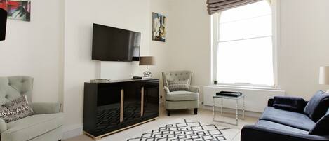 A modern living room with a grey sofa, a black entertainment unit, a beige armchair, and a patterned rug.
