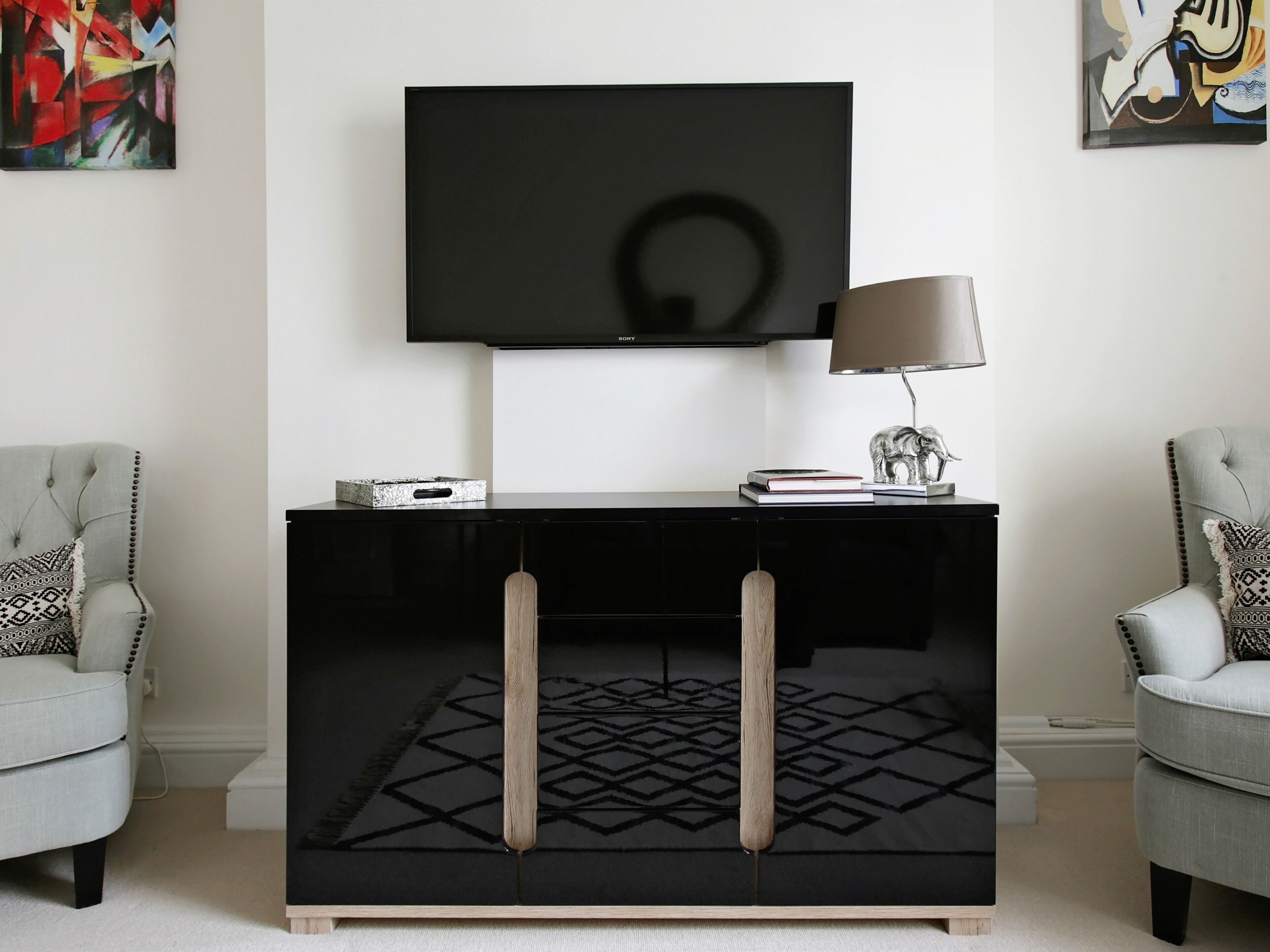 A modern living room with a black entertainment unit, a flat-screen TV, and two armchairs.