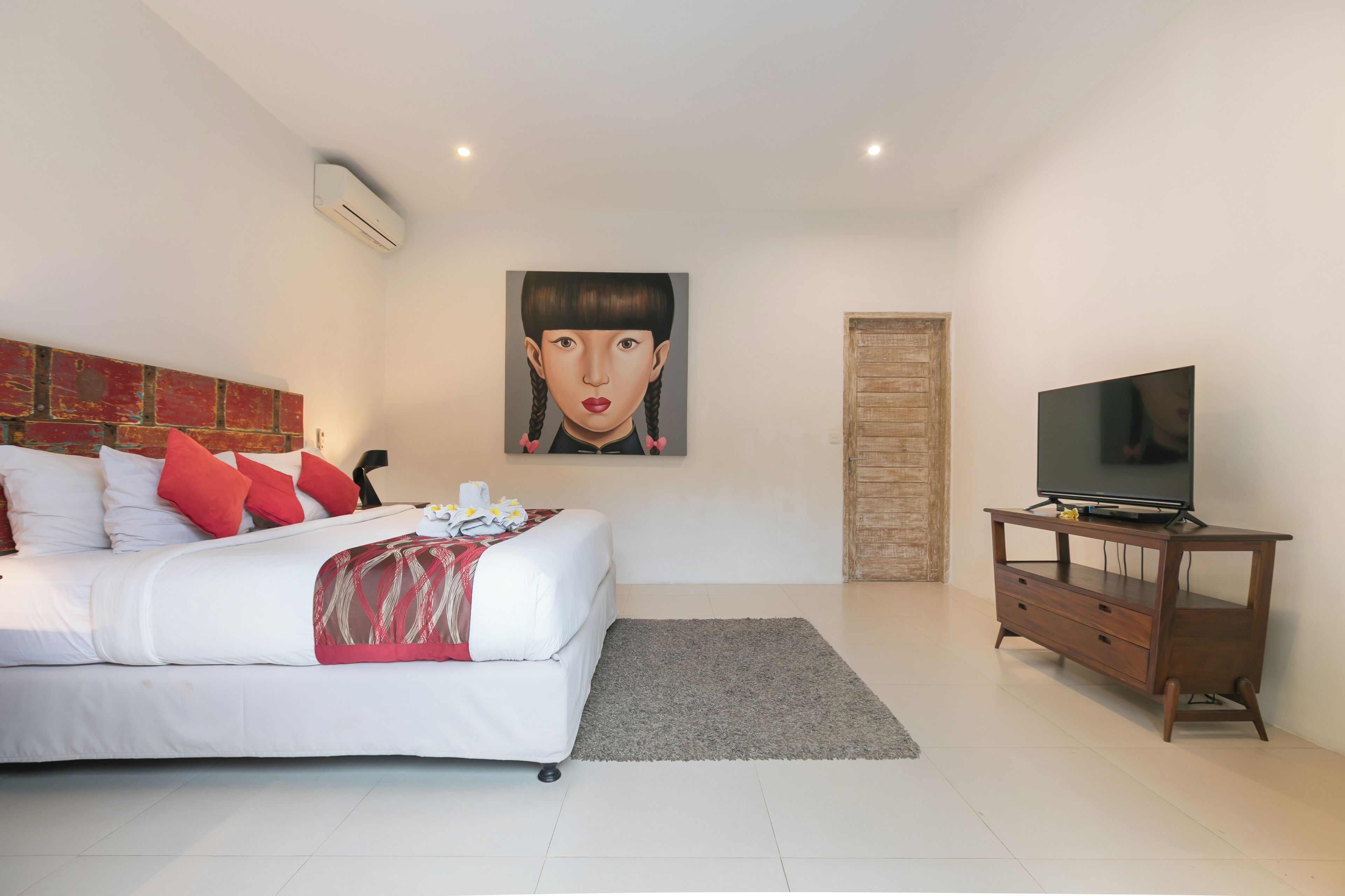 Une chambre à coucher avec un lit, un téléviseur posé sur un meuble en bois et un tableau accroché au mur.