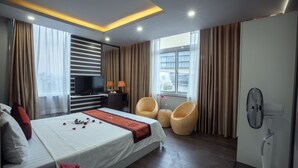 A modern hotel room with a large bed, a flat-screen TV, wicker chairs, and a fan. - Nam Long Hotel Ha Noi (Hanoi)