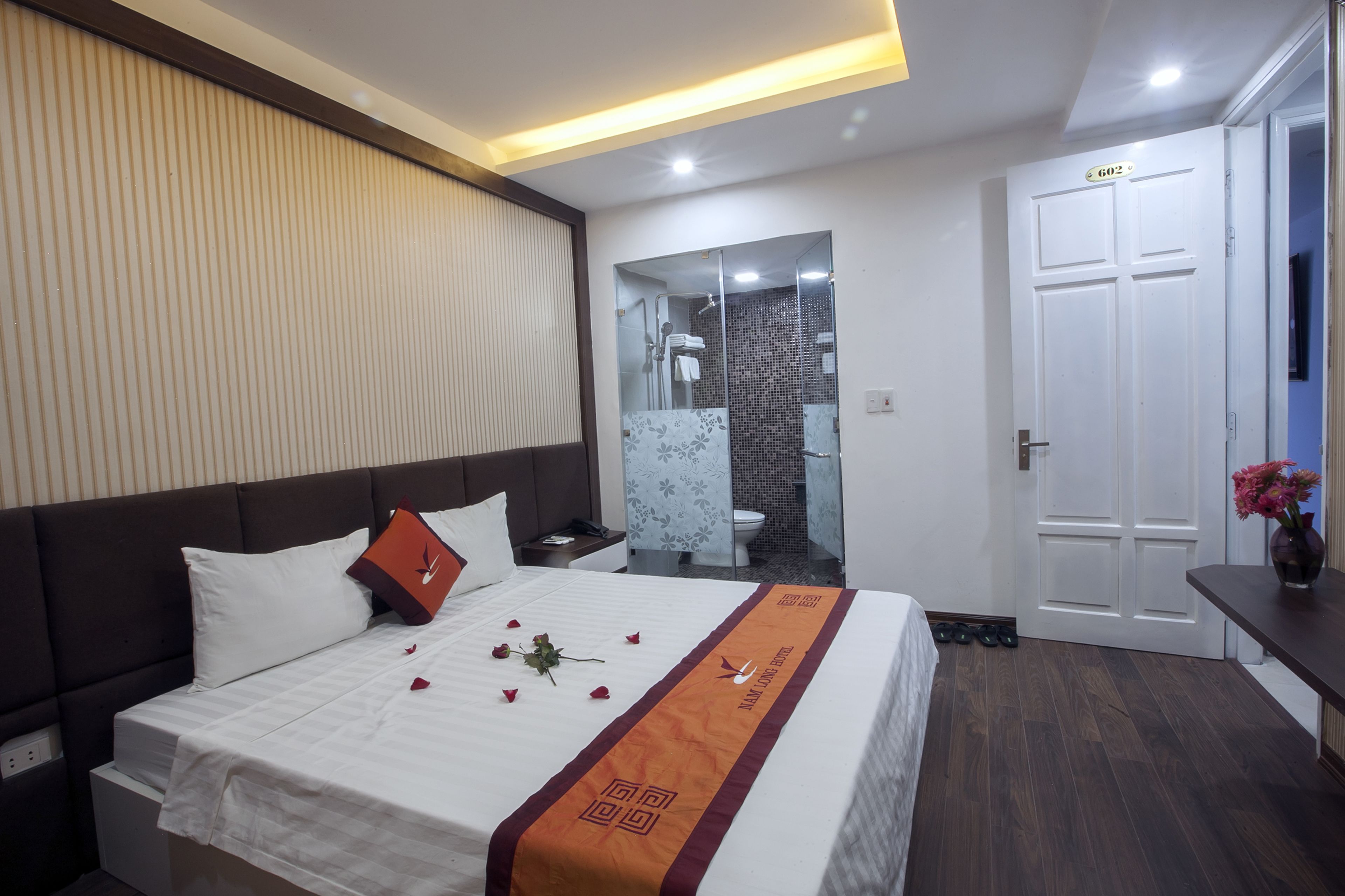 A hotel room with a neatly made bed, a bathroom with a glass shower enclosure, and a door marked with the number 602.